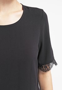 Svart t-shirt med rund halsringning och korta ärmar, prydd med spetsdetaljer vid ärmsluten. Mjuk tyg med en slät textur.