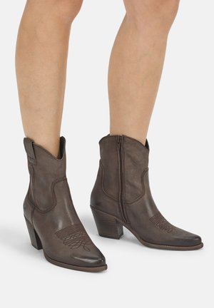 Bruine leren enkellaarzen met westernstijl, decoratieve stiksels op de tenen, zijrits en blokhakken gedragen op blote benen.