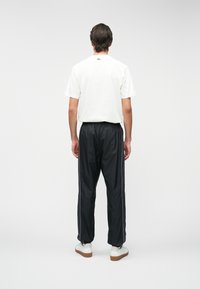 Λευκό βαμβακερό T-shirt, μαύρο αθλητικό παντελόνι με πλαινές ρίγες και λευκά αθλητικά παπούτσια με καφέ σόλα. Απλός, κανονικός σχεδιασμός.