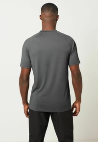 Grå atletisk t-shirt med korte ærmer, raglan-design og struktureret stof. Har en rund halsudskæring og en afslappet pasform, båret med sorte bukser.