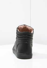 Černé vysoké tenisky s hladkým koženým povrchem, polstrovaným límcem a měkkým růžovým podšívkou. Texturovaná gumová podrážka zajišťuje přilnavost.