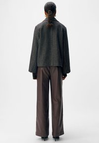 Schwarz-weiß gemusterte, kurz geschnittene Jacke mit weiten Ärmeln, kombiniert mit hochtaillierten braunen Hosen und schwarzen spitzen High Heels.