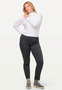 Weißer Rippstrickrollkragenpullover kombiniert mit dunkelgrauen, schmal geschnittenen Hosen mit Seitenreißverschlusstaschen und beigen Ankle Boots.