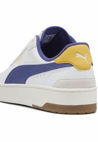 White leather sneaker with blue and yellow accents, textured heel, and rubber sole. Features classic Puma logo and perforated design for breathability.