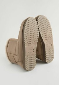 Stivali alla caviglia isolati beige con suola in gomma testurizzata e fodera morbida. La parte superiore presenta un design trapuntato con cuciture visibili.