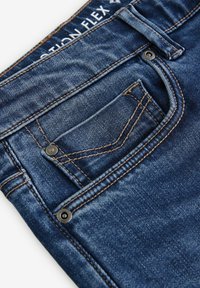 Vaqueros de mezclilla en azul oscuro con una textura suave. Sus características incluyen un pequeño bolsillo frontal, costuras en contraste en color marrón y detalles de metal.