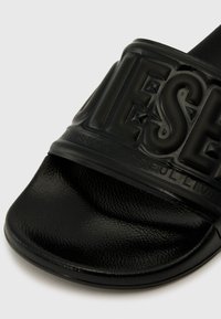 Sandale noire à bride, avec une tige en caoutchouc texturé portant un logo en relief et une semelle intérieure douce et ergonomique pour le confort.