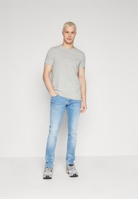 Camiseta gris de manga corta con logo, combinada con jeans azul claro y zapatillas grises. Diseño simple, ajuste casual, textura suave.
