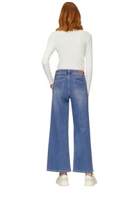 Brede blauwe denim jeans met een hoge taille, voorzien van een beige leren label, vijf zakken en een rafelige zoom, gecombineerd met witte sneakers.