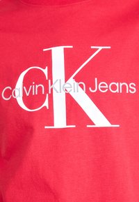 Rode katoenen t-shirt met groot wit "CK" logo en "Calvin Klein Jeans" tekst in grijs, met een ronde halslijn en een gladde textuur.