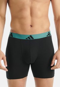 Černé boxerky s těsným střihem a turquoisovým elastickým pasem, na kterém je černé logo Adidas, navržené pro pohodlí a podporu.