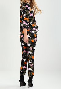 Ensemble floral avec un fond noir et des fleurs multicolores en rose, blanc et orange. Comprend un haut fluide et un pantalon ajusté.