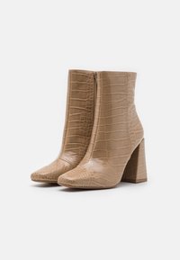 Bottes de cheville en cuir d'alligator de couleur beige clair, avec un bout pointu, un talon bloc et une fermeture à glissière sur le côté. Texture lisse.