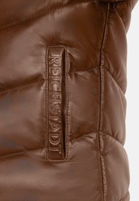 Giacca di pelle marrone con un design trapuntato e lettering in rilievo "REICHSTADT" sul lato, che evidenzia una texture liscia e un'imbottitura consistente.