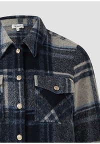 Dunkelblaues und grau kariertes Wollhemd mit silbernen Knöpfen und einer Brusttasche mit einem geknöpften Überschlag, Kragen sichtbar.