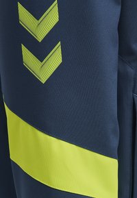 Marinblå prestandabyxor med ett texturerat gult rand och en chevrongrafik. Har ett slätt tyg och kontrasterande sömmar.