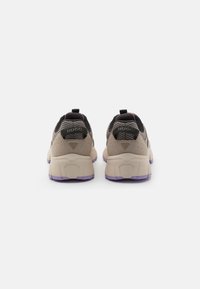 Sneakers med en svart mesh-överdel, ljusbeige mockadetaljer och en kraftig vit sula med en lila gummisula. Varumärkeslogotyp på hälen.