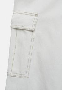 Tissu en denim blanc avec une poche plaquée dotée de coutures visibles et d’une surface texturée. La poche est rectangulaire et possède un rabat.