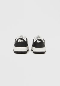 Fekete bőrcipők fehér fűzővel, gumitalppal és kontrasztos fehér varrással, a sarkon márkázott krokodil logóval.