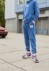 Blaues Hoodie und Jogginghose mit einem verblassten Muster und Jordan-Logo-Patch; kombiniert mit bunten Sportschuhen mit rosa und schwarzen Akzenten.