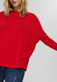Rød strikketrøje med et struktureret striped mønster, løs pasform, bred halsudskæring og dropped skuldre, parret med blå jeans.