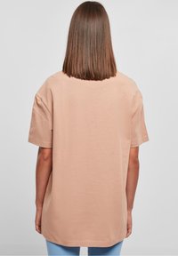 Světle béžové oversized tričko s krátkým rukávem, měkká bavlněná textura a kulatý lem, zobrazené zezadu.