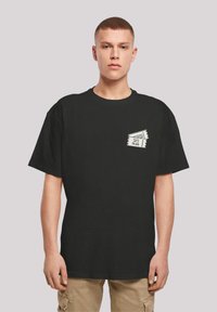 Black cotton t-shirt with short sleeves, featuring a front chest pocket design of a ski pass in white outline. Casual fit, smooth texture.