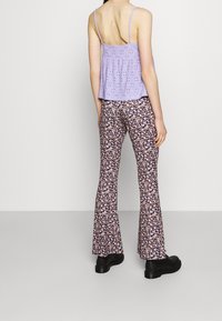 Lila ärmlös topp med hålmönster; blommig, utsvängd byxor; svarta klumpiga skor. Bakgrunden är neutral grå.