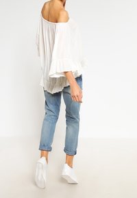 Vit off-shoulder topp med volangärmar, kombinerad med ljusblå uppvikta jeans och vita slip-on sneakers. Texturerad tyg och avslappnad passform.