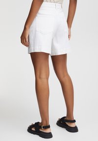 Pantaloni corti bianchi in misto cotone con risvolti, due tasche posteriori e vita alta. Abbinati a sandali neri piatti con fibbia.