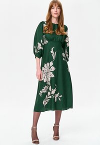 Zielona sukienka maxi z bufiastymi rękawami, ozdobiona dużymi beżowymi wzorami kwiatowymi. Wykonana z gładkiej tkaniny, o luźnym kroju i okrągłym dekolcie.