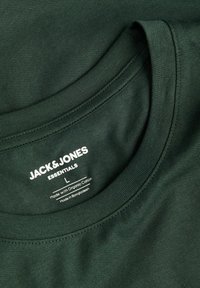 Σκούρο πράσινο T-shirt με στρογγυλή λαιμόκοψη, κατασκευασμένο από οργανικό βαμβάκι. Διαθέτει ετικέτα με το όνομα της μάρκας, το μέγεθος και οδηγίες φροντίδας.