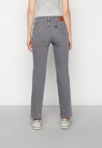 Grijze denimjeans met een rechte pijp, met achterzakken en een bruine leren label op de tailleband. Zoom is iets rafelig aan de onderkant.