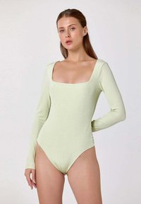 Body à manches longues de couleur vert pâle, avec un décolleté carré, une coupe ajustée et une texture côtelée. Convient à diverses occasions.