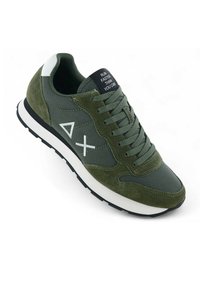 Scarpa sportiva verde in una combinazione di materiali scamosciati e tessili. Accenti bianchi e un'etichetta nera sulla linguetta con del testo.