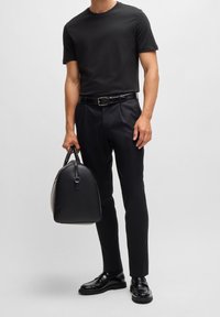 Černé tričko s krátkým rukávem, černé elegantní kalhoty, lesklé černé boty a černá kožená taška s oblé tvarem a pevnými uchy.