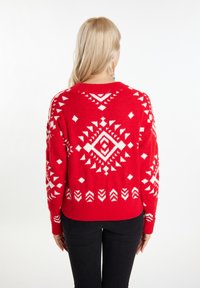 Pulover roșu cu un model geometric alb, mâneci lungi, țesătură texturată și un guler rotund, asortat cu pantaloni negri.