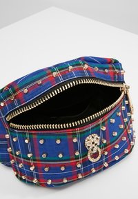 Rutig mönster väska i blått, rött och grönt med guldfärgade nitar, en dekorativ rund spänne och dragkedjestängning. Fodrad med svart tyg inuti.