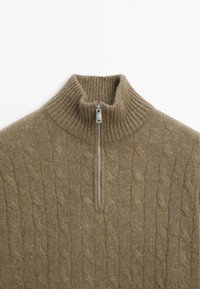 Maglione marrone a treccia con un alto colletto a coste e una piccola cerniera sul collo. Texture morbida e design rilassato.
