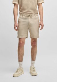 Bermuda beige in lino con vita regolabile, abbinate a sneakers beige e calze chiare, indossate con una maglietta coordinata e texturizzata.