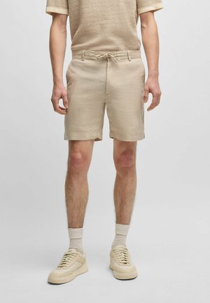 Shorts en lin beige avec une taille à cordon, associés à des baskets beige et des chaussettes claires, portés avec un haut texturé assorti.