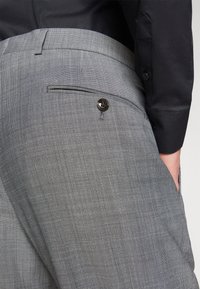 Graue Hose aus strukturiertem Stoff, mit einer Gesäßtasche und einem schwarzen Knopfdetail sowie einem dezenten Karomuster.
