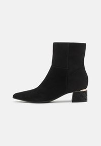 Stivaletti ankle in suede nera con punta affilata e tacco a blocco nero testurizzato con accento dorato. Finitura liscia e design aderente.