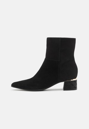 Stivaletti ankle in suede nera con punta affilata e tacco a blocco nero testurizzato con accento dorato. Finitura liscia e design aderente.