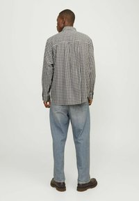 Camisa de cuadros con cuello, en tonos de azul y blanco, combinada con jeans holgados de color azul claro y zapatos marrón oscuro.