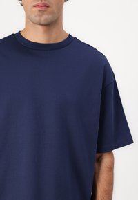 Granatowa koszulka z krótkim rękawem wykonana z bawełny, z okrągłym dekoltem i luźnym krojem o gładkiej fakturze. Minimalistyczny design.
