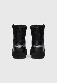 Botas altas negras para niños con un tejido brillante, cuellos acolchados y "KARL LAGERFELD KIDS" impreso en las lengüetas del talón.
