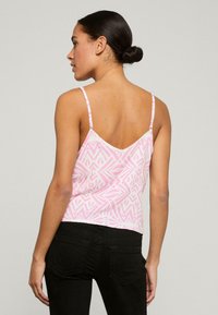 Top senza maniche rosa con motivo geometrico, design a V sul retro e spalline sottili. Realizzato in tessuto leggero; abbinato a jeans neri.