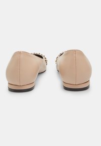 Ballerine in pelle beige con tacco basso, caratterizzate da borchie decorative in tono oro lungo l'apertura, texture liscia e dettagli cuciti.