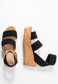 Schwarze Keilsandalen mit drei breiten Stoffriemen. Korkmuster auf dem Keilabsatz. Glattes, sandfarbenes Fußbett. Leichtes, offenes Design.